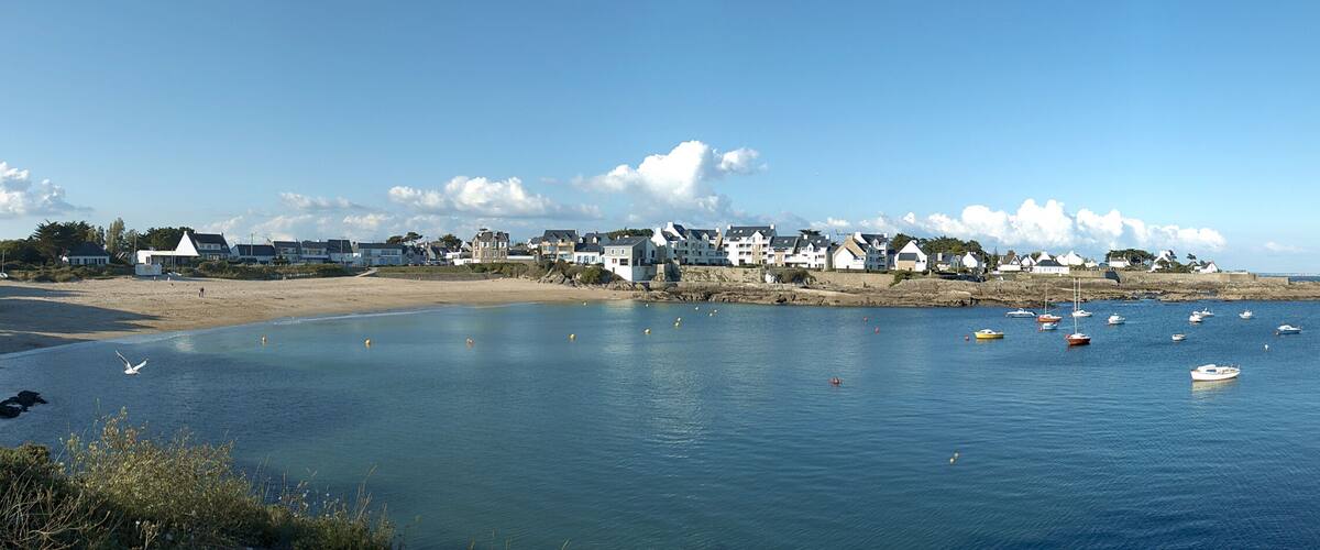 A coastal town with houses along the shore, boats in the water, and a clear sky.