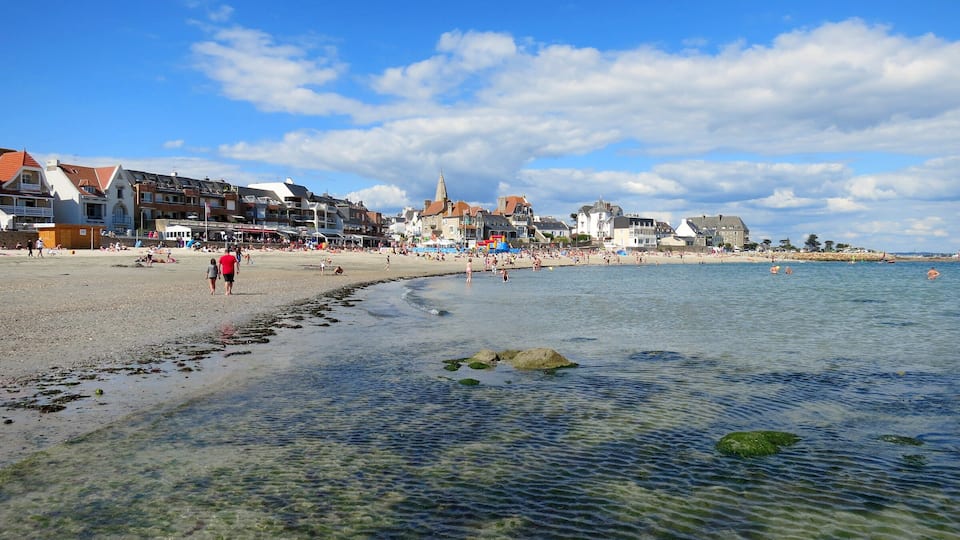 A beach with clear water, people, and buildings along the shore.