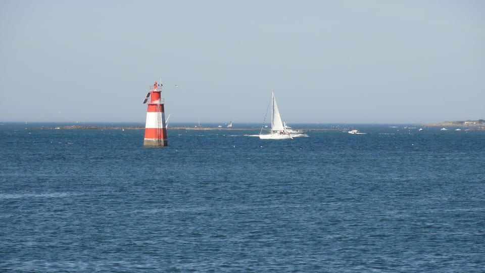 A lighthouse, a sailboat, and several other boats on the water.