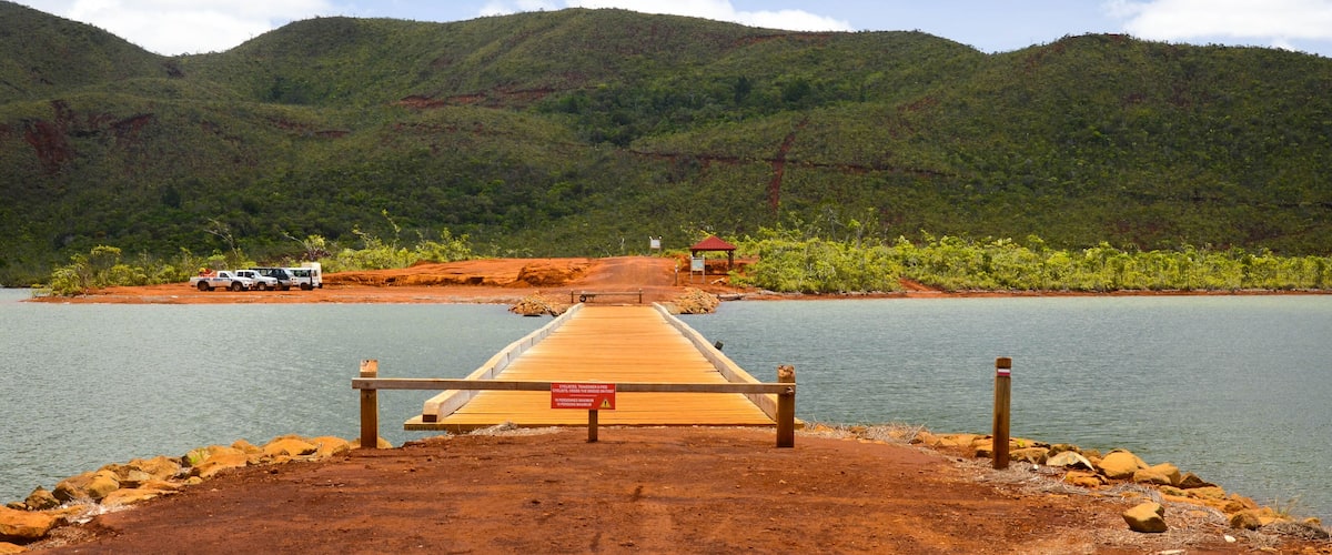 A wooden dock leading to a calm lake surrounded by green hills.