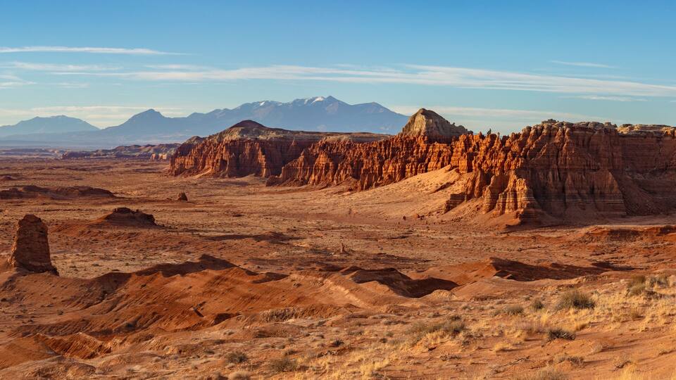 A desert landscape with prominent red rock formations and distant mountains under a clear sky.