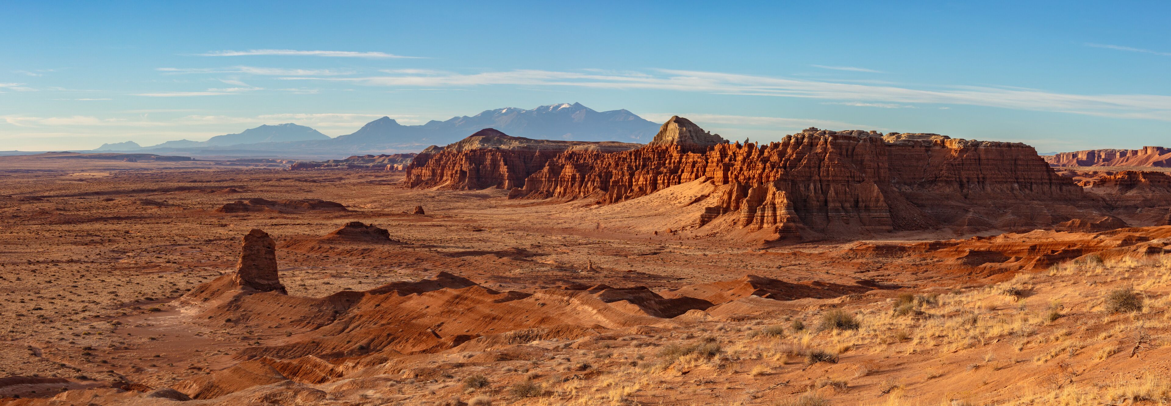 A desert landscape with prominent red rock formations and distant mountains under a clear sky.