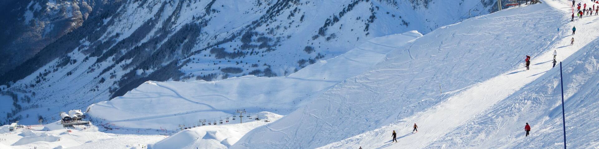 Skiers are sliding down snow-covered hill on skis at the Cirque du Lys. There is range of mountains (Soum de Mauloc) in the background
