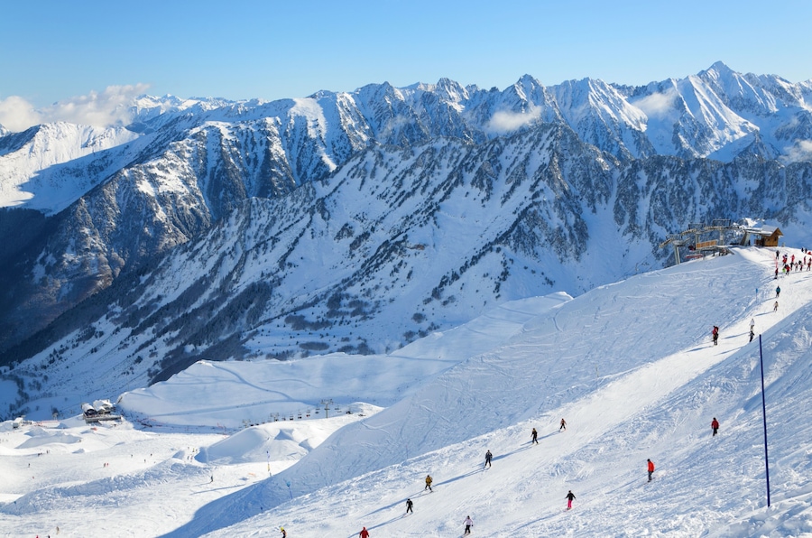 Skiers are sliding down snow-covered hill on skis at the Cirque du Lys. There is range of mountains (Soum de Mauloc) in the background