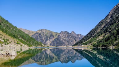 Um lago de montanha com reflexos nítidos, rodeado por encostas florestadas e picos rochosos.