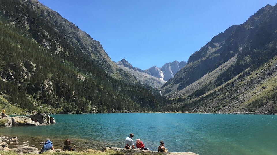 A group of people sitting by a lake surrounded by mountains.