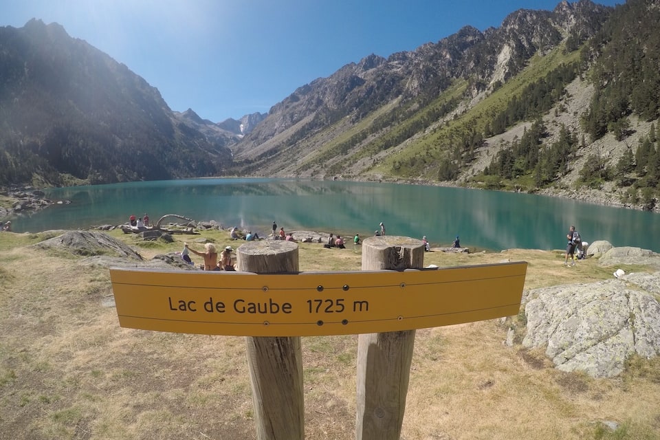 Schild, das Lac de Gaube in 1725 Metern Höhe zeigt, umgeben von Bergen und einem türkisblauen See mit Menschen.