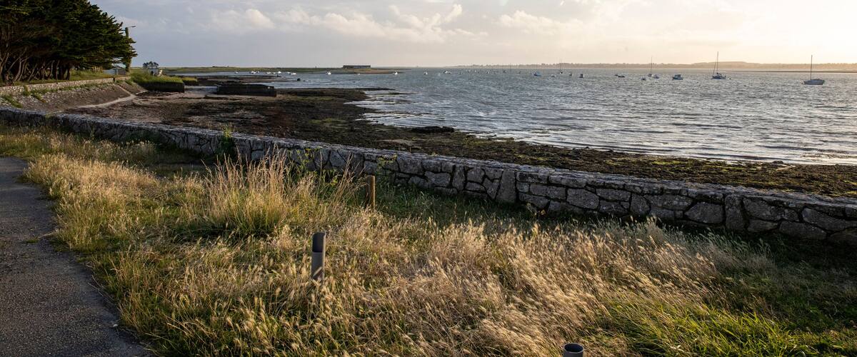A coastal landscape with a stone wall, grassy area, and boats on the water.