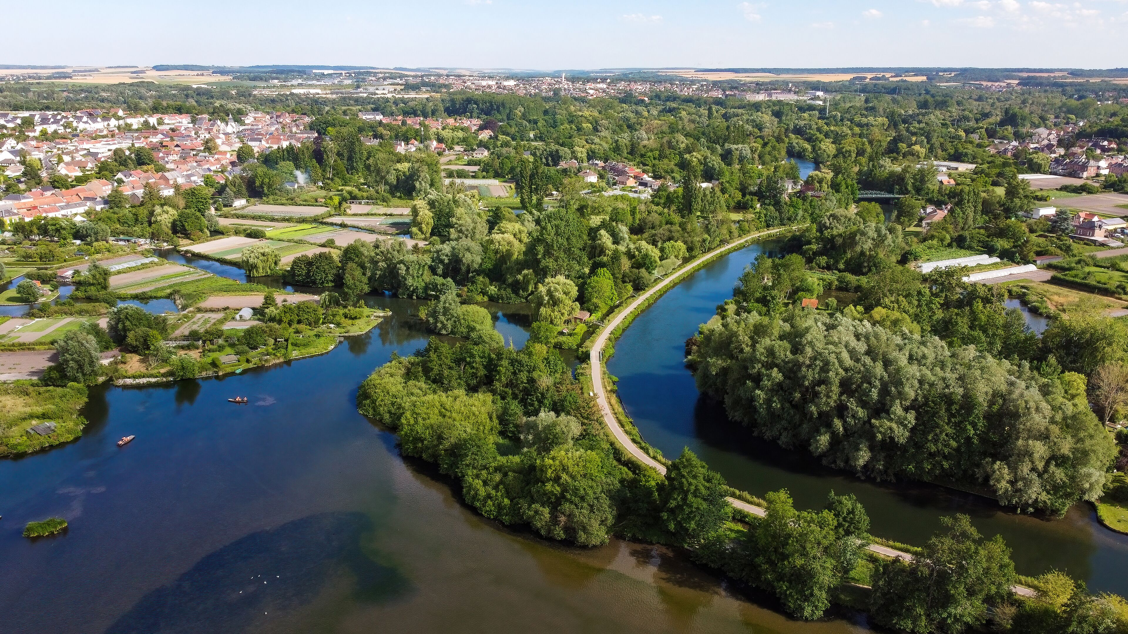 A river winding through a densely wooded area with residential buildings and fields.