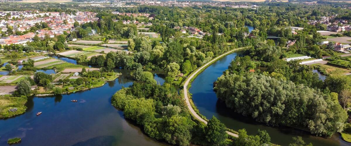 A river winding through a densely wooded area with residential buildings and fields.