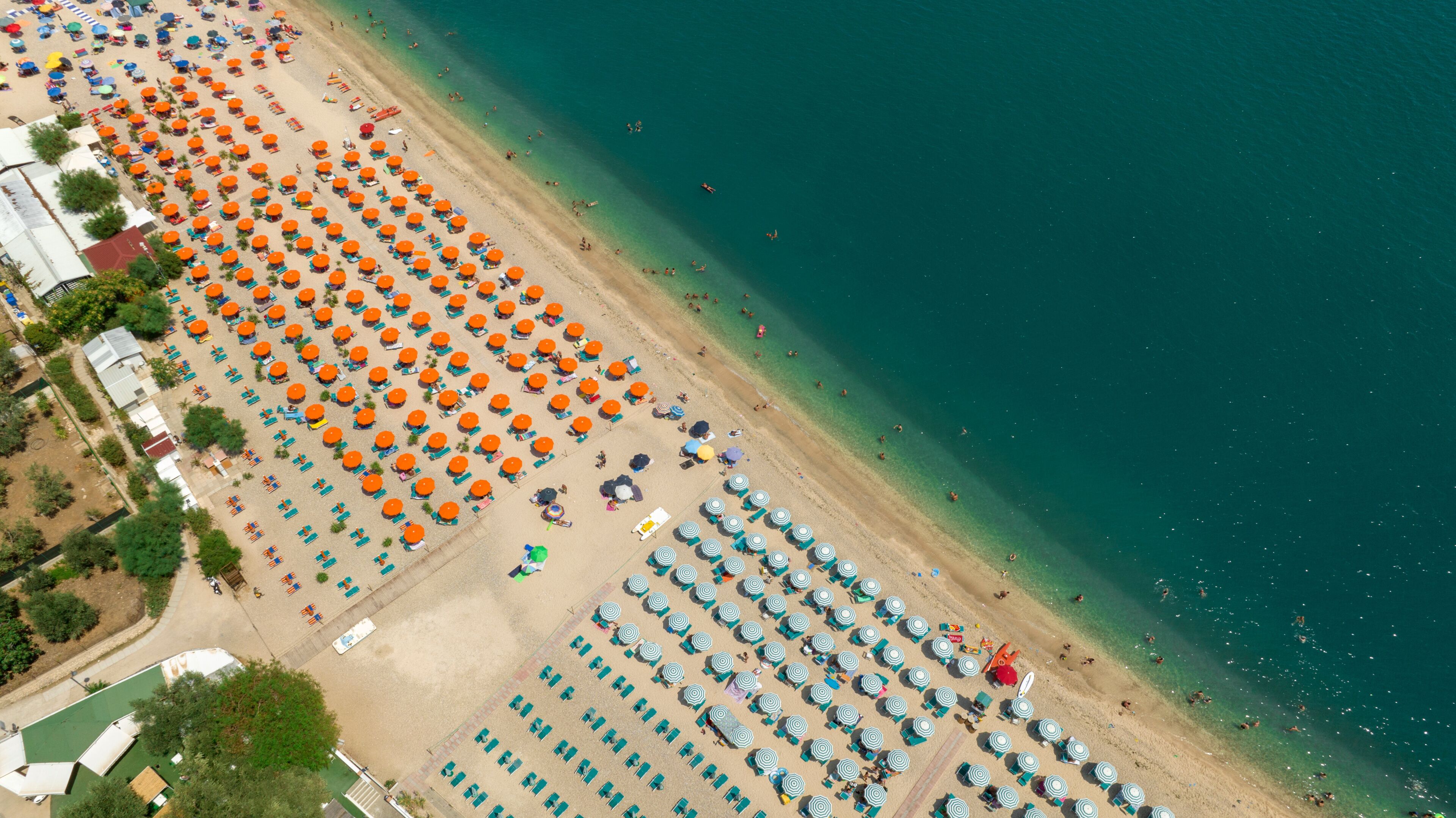 An aerial view of a beach with rows of sun umbrellas and lounge chairs.