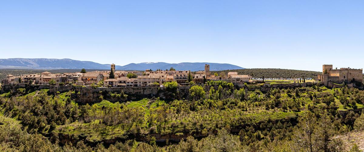 A historic town perched on a hillside with medieval architecture, surrounded by mountains and dense forests.