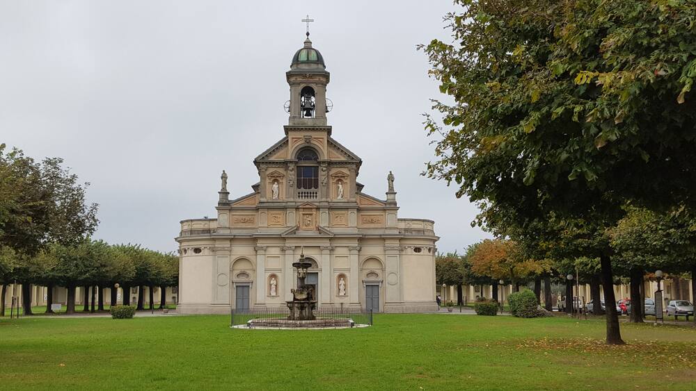 Une église dotée d’un clocher et d’une fontaine, située au centre d’une cour verdoyante.