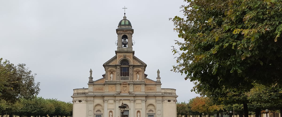 A church with a bell tower and a fountain in the center of a grassy courtyard.