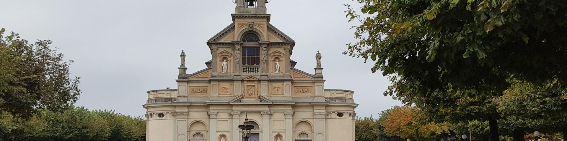 A church with a bell tower and a fountain in the center of a grassy courtyard.