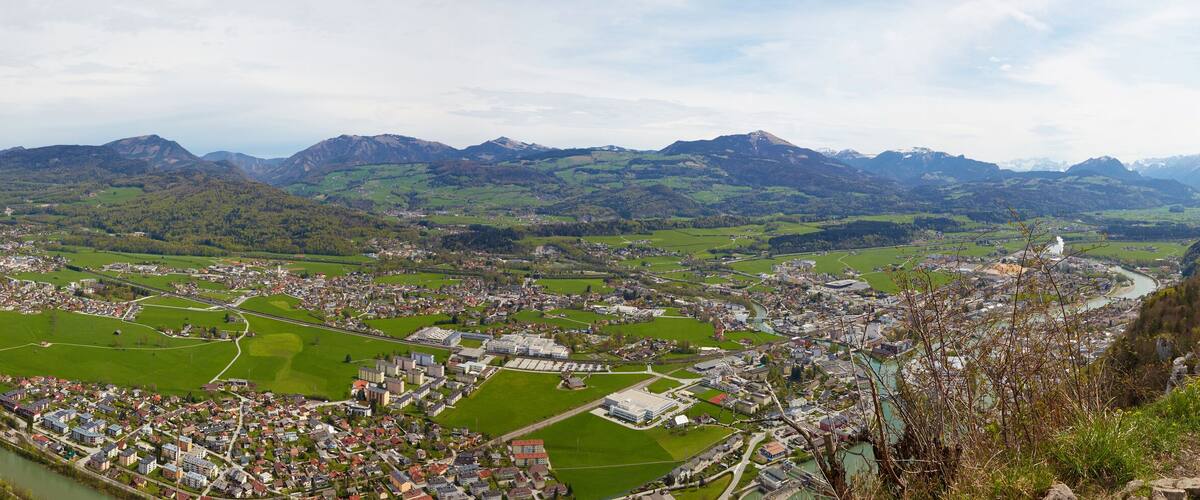 A panoramic view of a town nestled in a valley with a river running through it, surrounded by mountains.