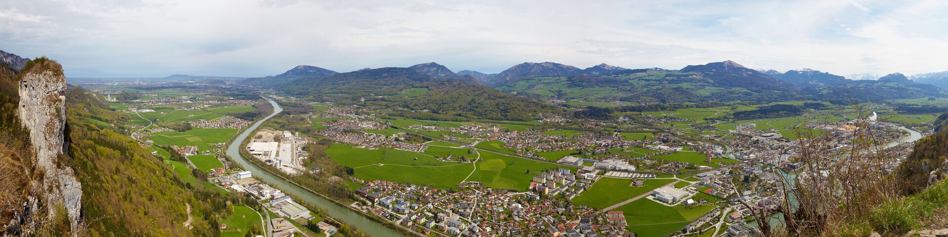 A panoramic view of a town nestled in a valley with a river running through it, surrounded by mountains.