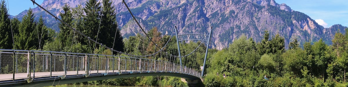 A suspension bridge over a calm river with a mountain backdrop.