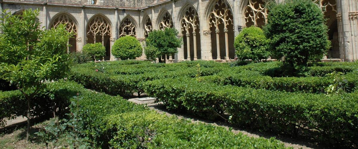 A historic building with arched windows and a courtyard with neatly trimmed hedges.