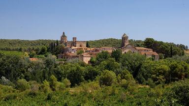Un pueblo histórico con arquitectura medieval, rodeado de exuberante vegetación y colinas.