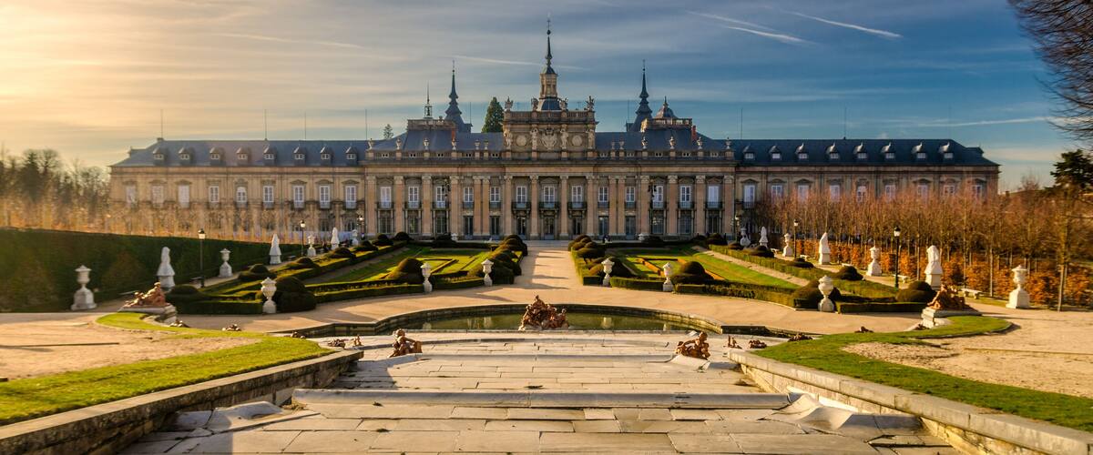 A grand palace with a symmetrical garden, a central fountain, and statues lining the pathways.