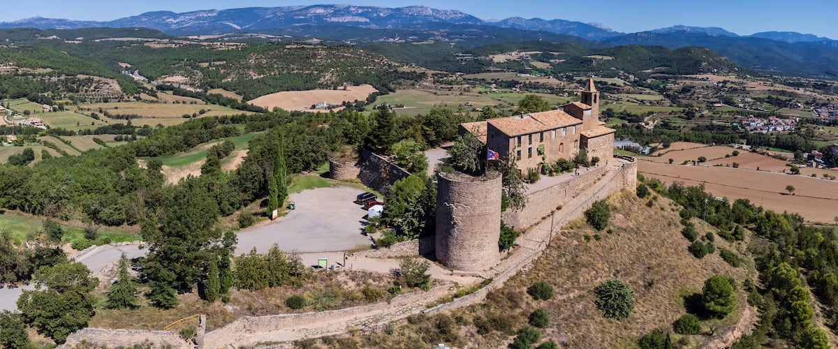 A medieval castle with a tower, surrounded by rolling hills and a clear blue sky.
