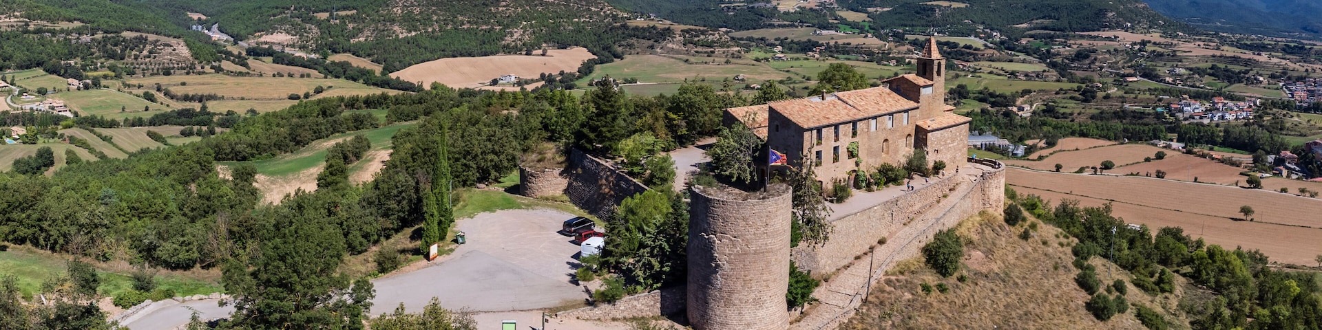 A medieval castle with a tower, surrounded by rolling hills and a clear blue sky.