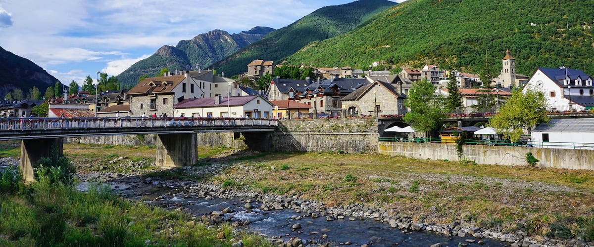 A bridge over a river, a town with historic buildings, and mountains in the background.