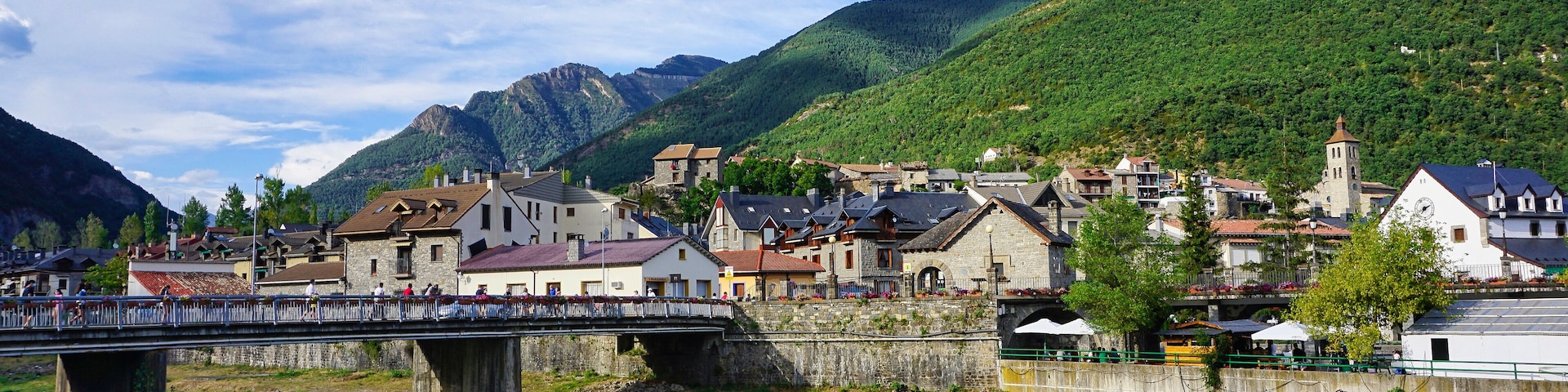 A bridge over a river, a town with historic buildings, and mountains in the background.