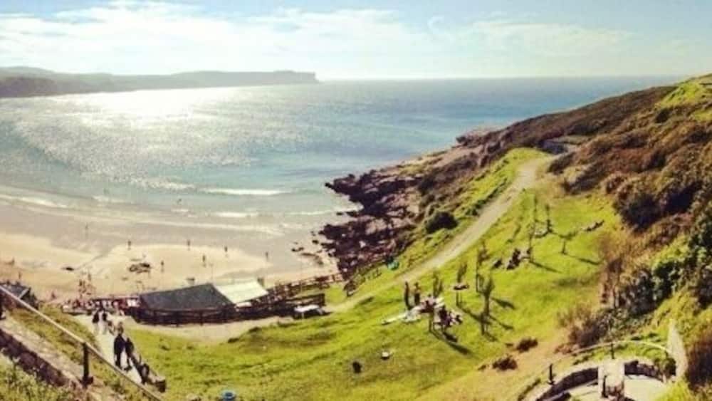 Un paysage côtier avec une plage, des collines verdoyantes et un bâtiment situé sur une colline.