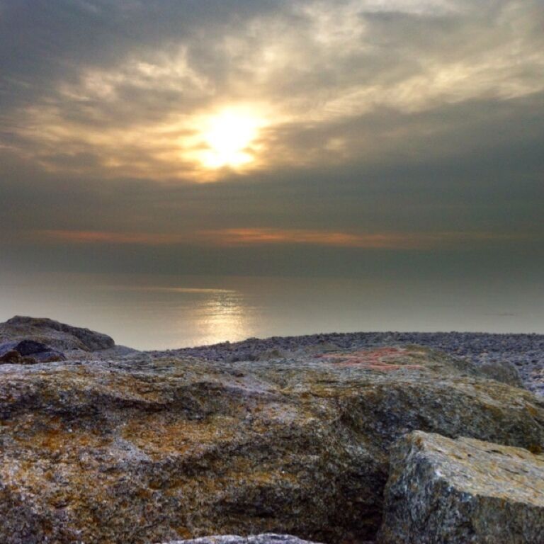 A rocky shoreline with a sunset over a calm body of water.