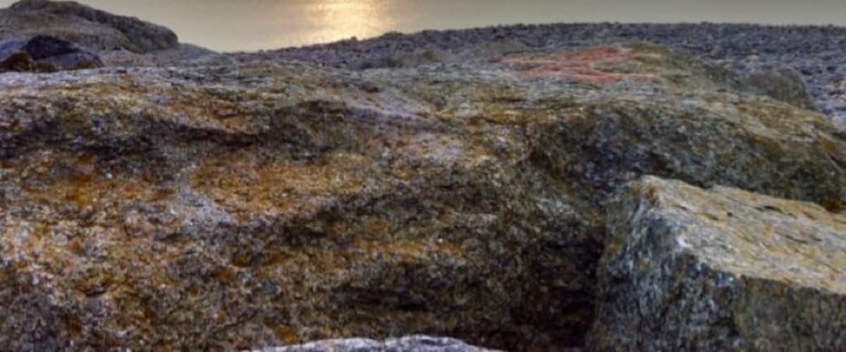 A rocky shoreline with a sunset over a calm body of water.