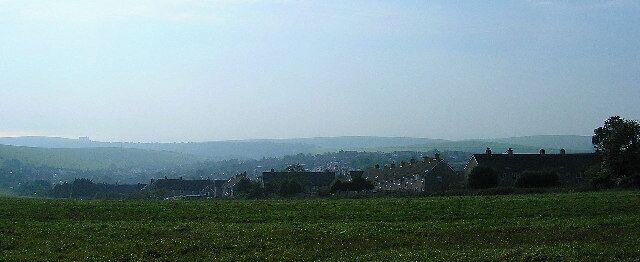 A rural landscape with rolling hills, scattered houses, and a clear sky.