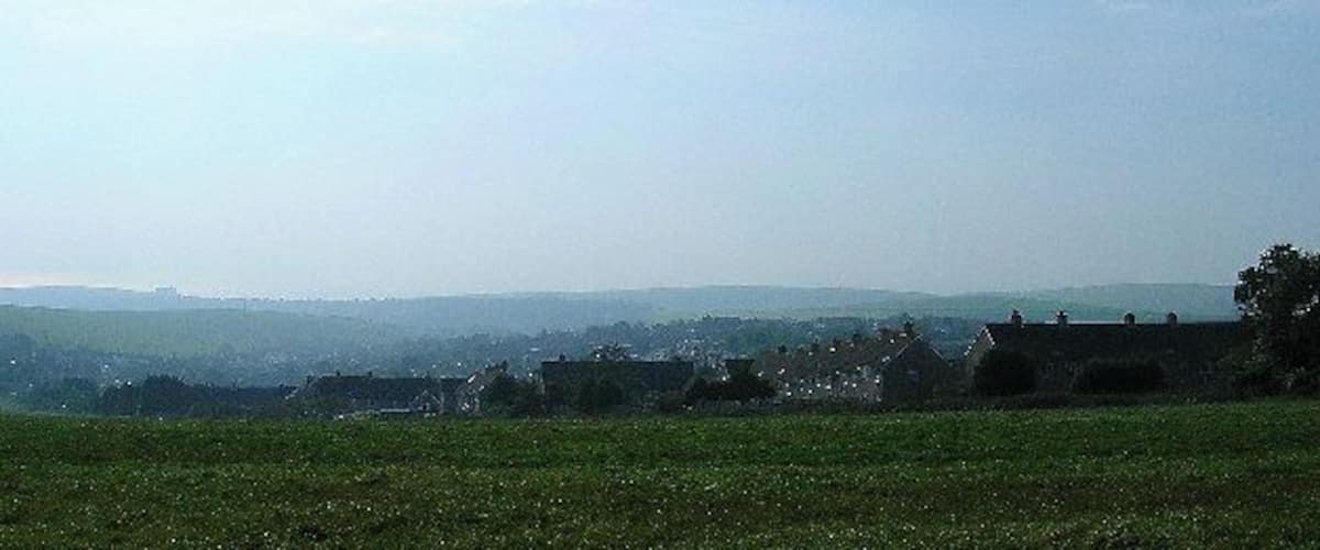 A rural landscape with rolling hills, scattered houses, and a clear sky.