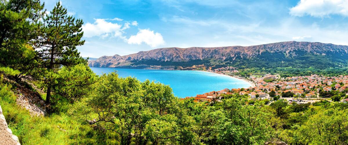 A coastal town with a mountain backdrop, surrounded by dense greenery.