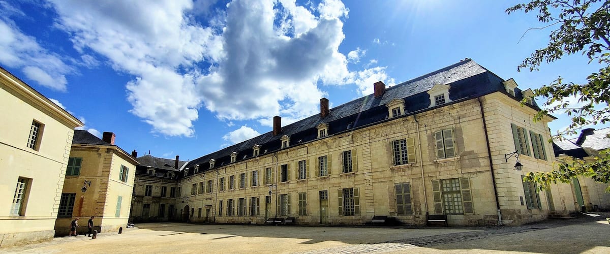 A historic courtyard with a large building featuring multiple windows and a cobblestone ground.