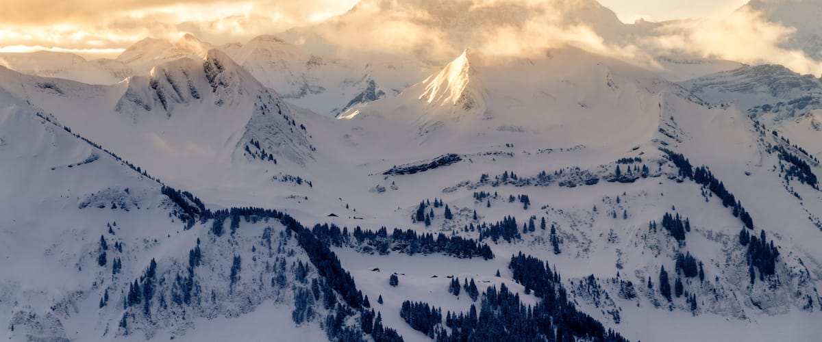 A snow-covered mountain range with a prominent peak and dense forests at its base.