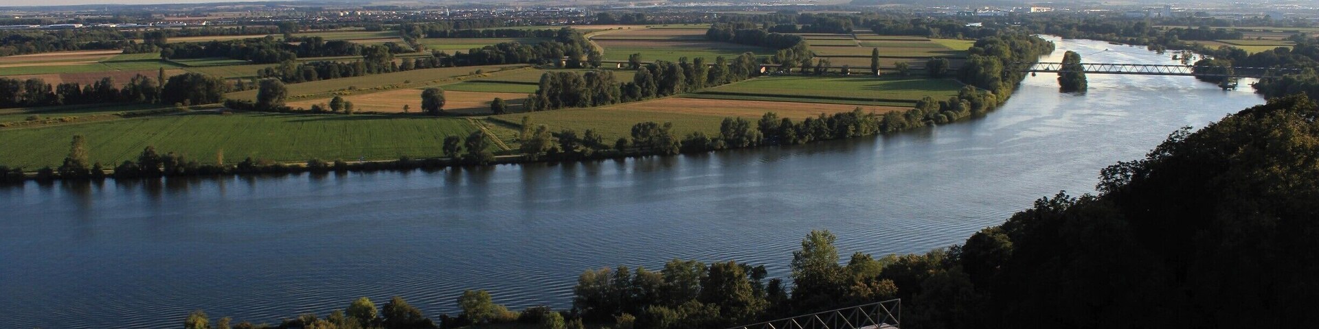 A river flowing through a rural landscape with fields and a bridge.