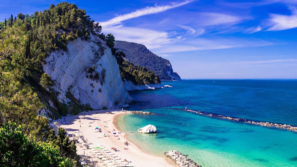 A coastal landscape with a white sandy beach, clear turquoise waters, and a rocky cliff.
