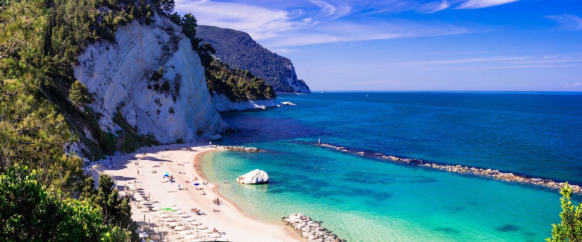 A coastal landscape with a white sandy beach, clear turquoise waters, and a rocky cliff.