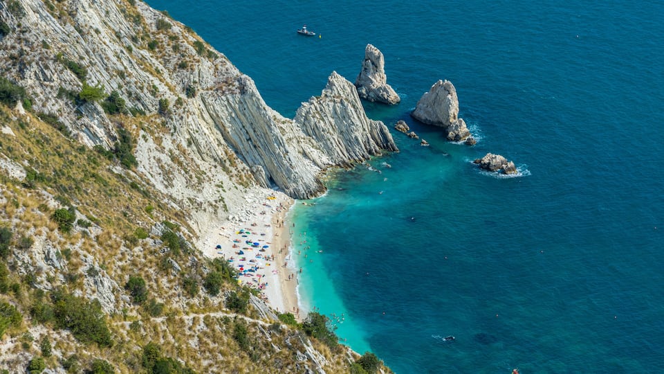 A coastal landscape with a rocky beach, clear turquoise waters, and a mountainous backdrop.
