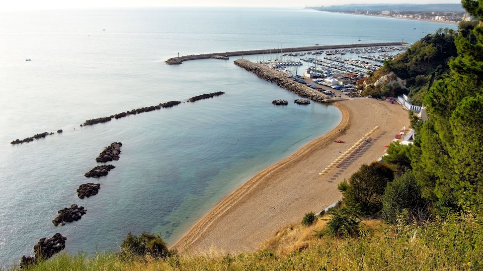 A coastal view with a sandy beach, a marina, and a rocky breakwater.