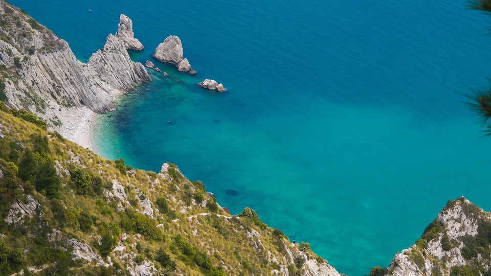 A coastal landscape with rocky cliffs, clear turquoise waters, and a narrow beach.