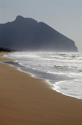 Una spiaggia con onde, una riva sabbiosa e una montagna sullo sfondo.