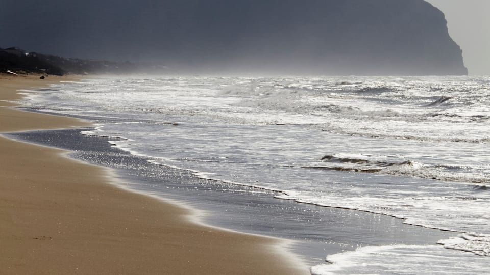 A beach with waves, a sandy shore, and a mountain in the background.