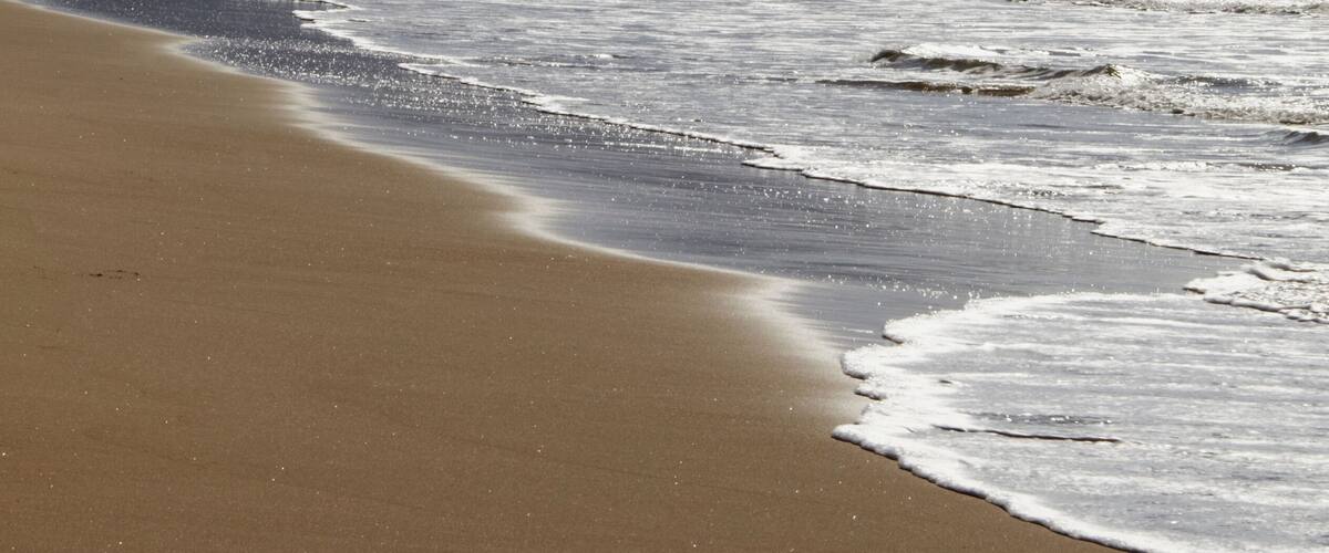 A beach with waves, a sandy shore, and a mountain in the background.