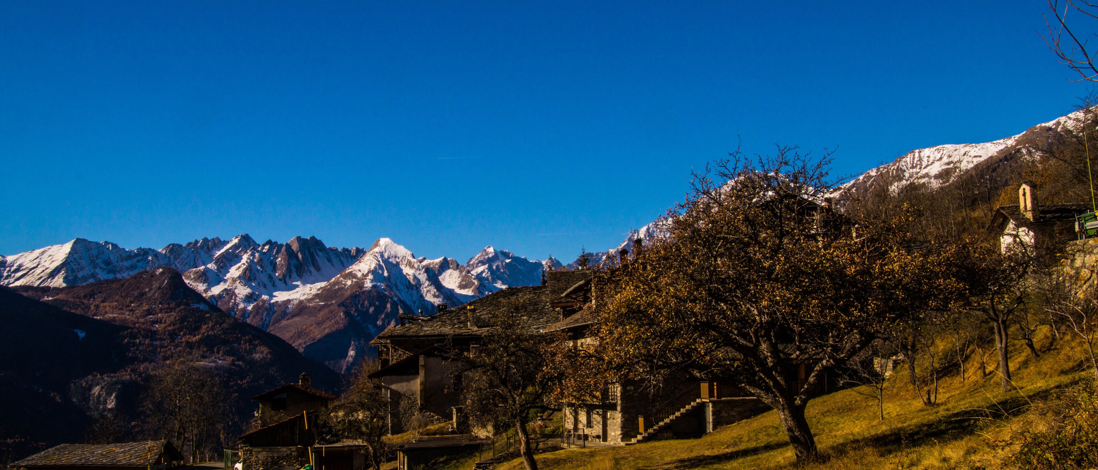 A mountainous landscape with snow-capped peaks, a village with traditional buildings, and a clear blue sky.