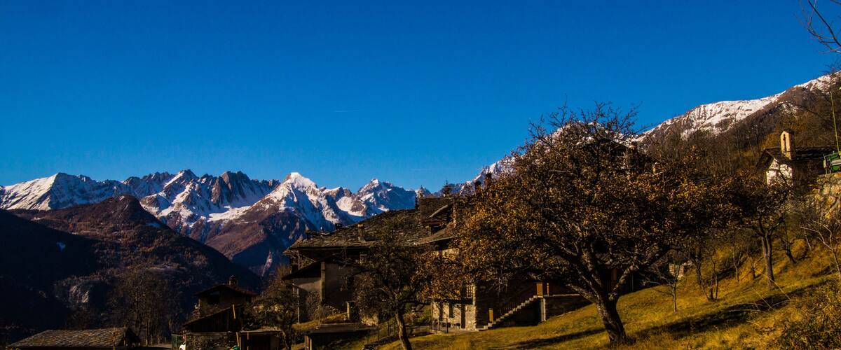 A mountainous landscape with snow-capped peaks, a village with traditional buildings, and a clear blue sky.