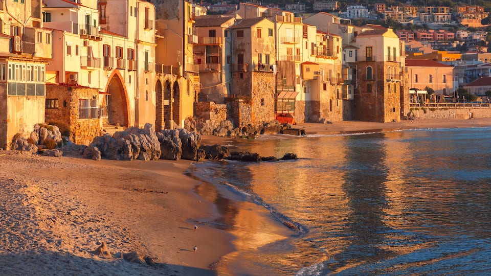 A coastal town with stone buildings, a sandy beach, and a calm sea.