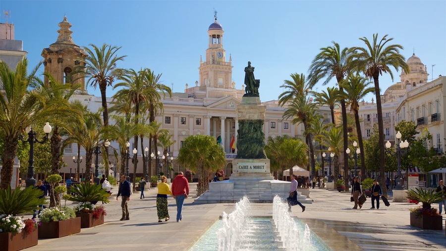 A plaza with a fountain, palm trees, and a statue.